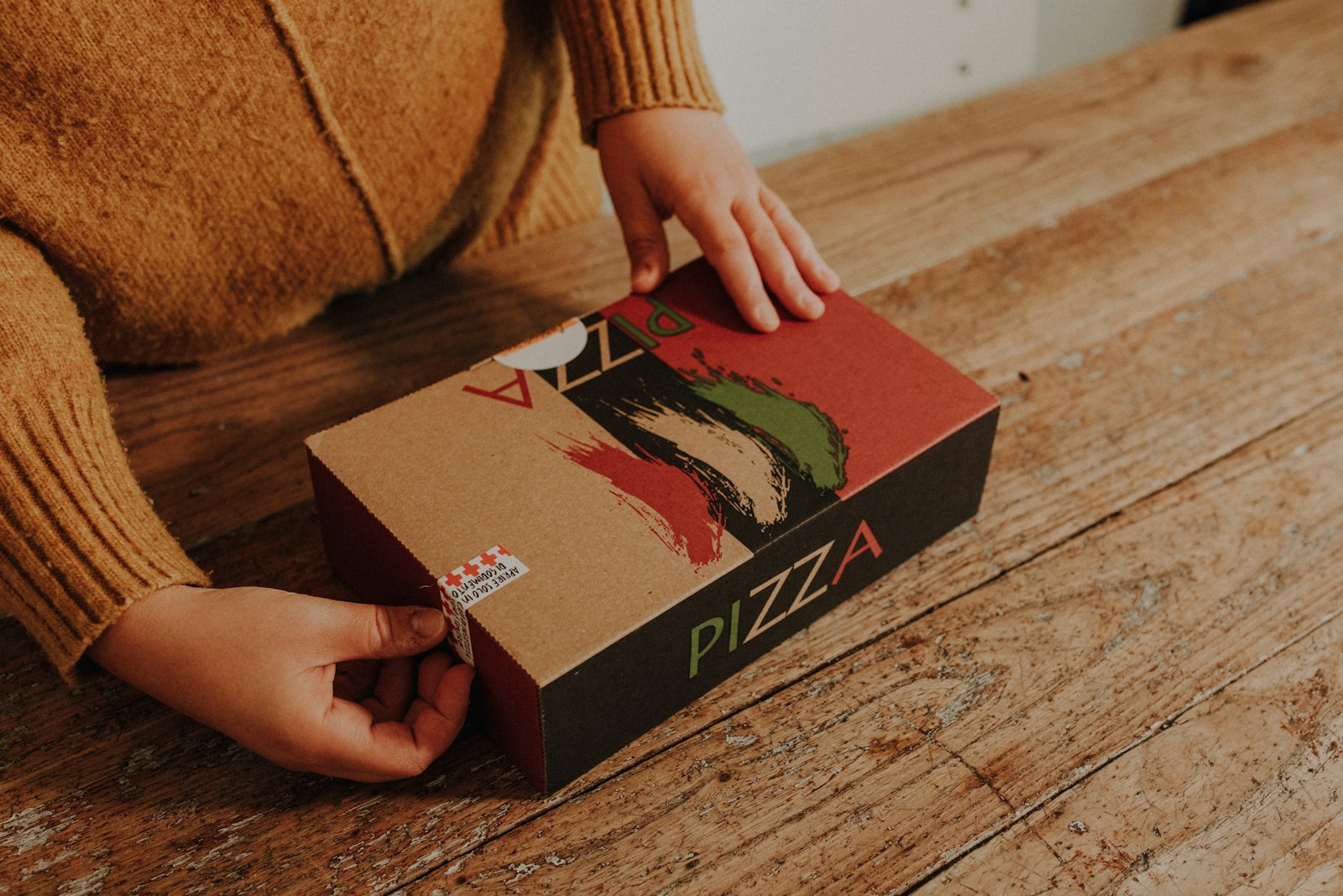 A person opening a pizza delivery box on a wooden table