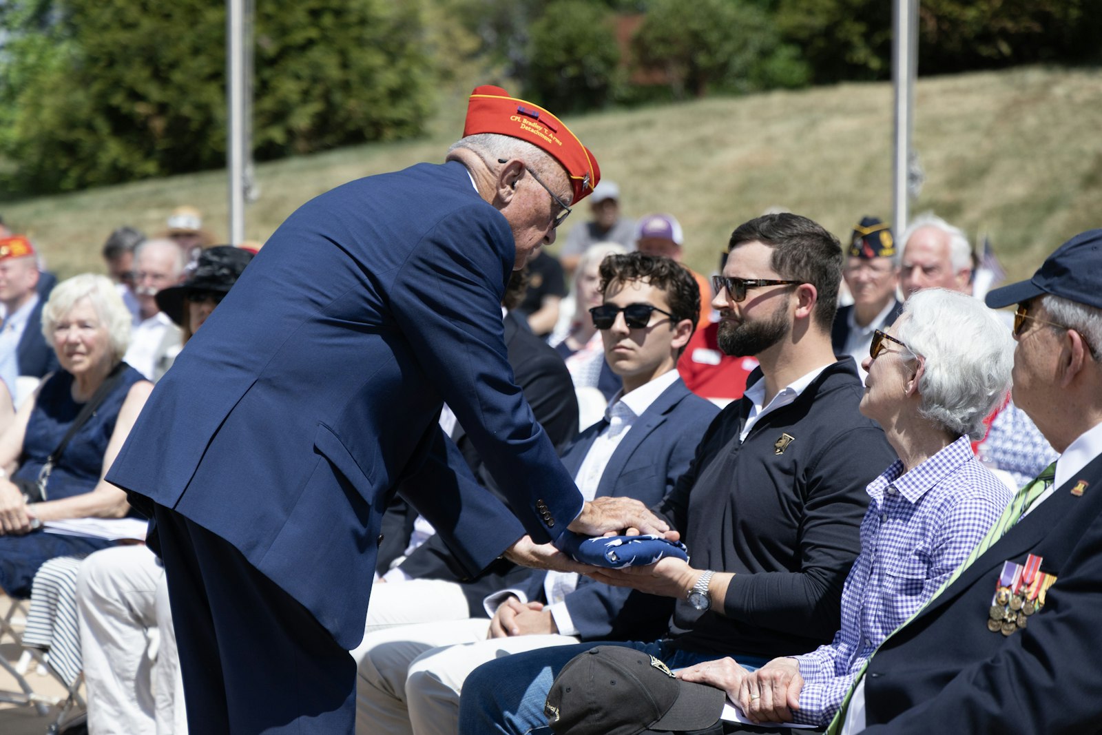 A military veteran presenting a folded American flag to a seated group at a ceremony