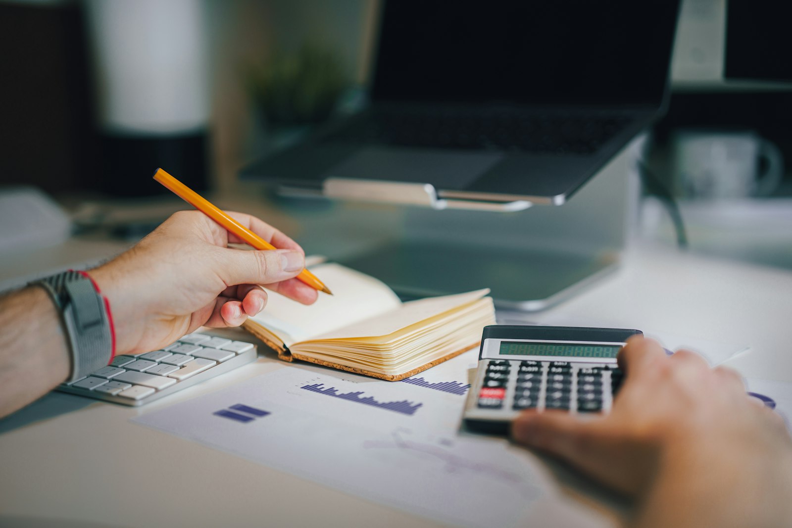 A person tracking expenses with a notebook, pencil, and calculator at a desk